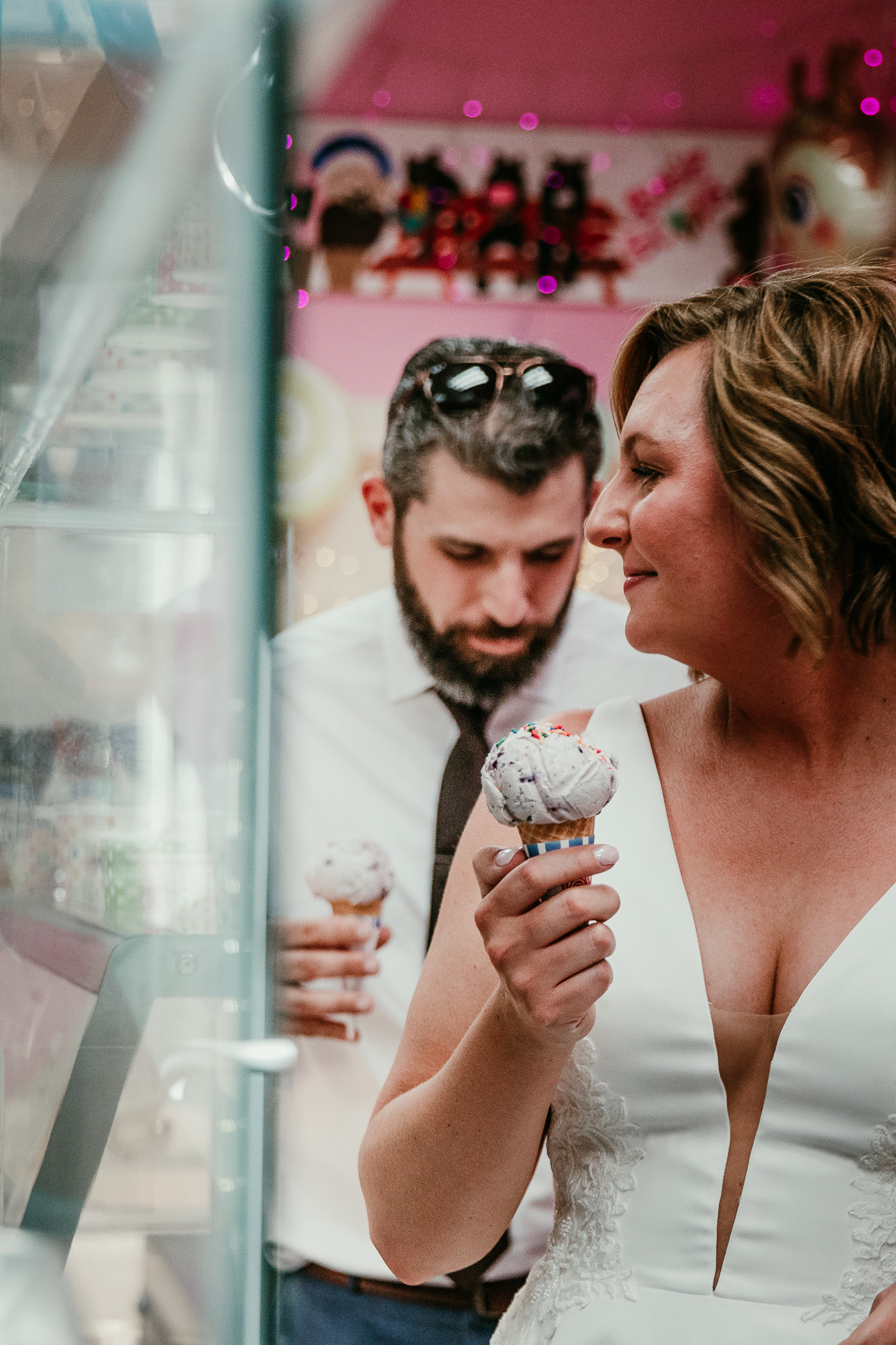 SJ smiling with her ice cream cone while Dave stands behind her in the shop.