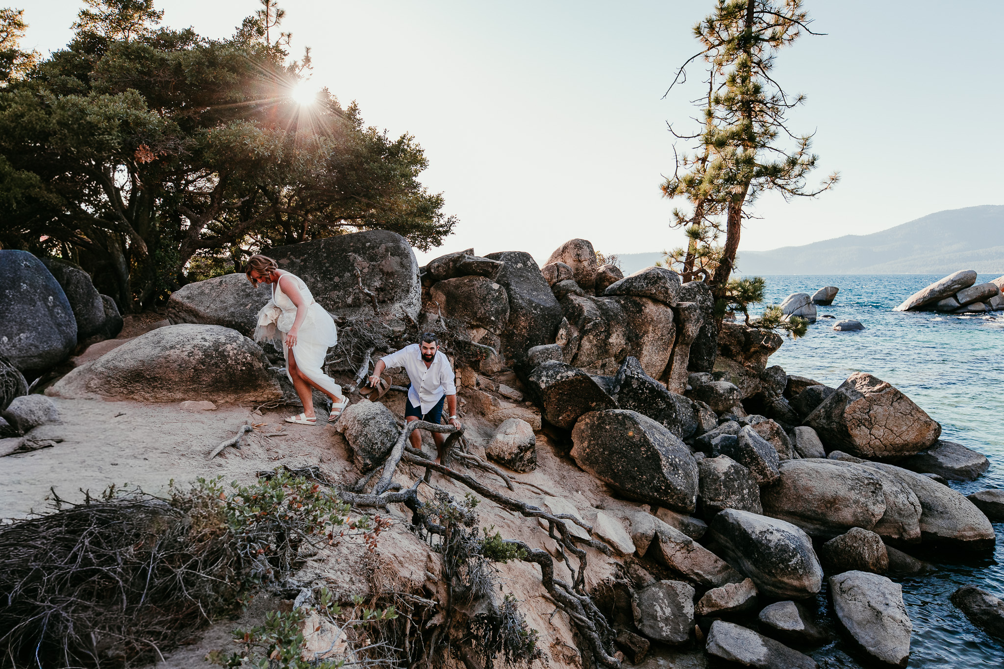 SJ and Dave exploring the rocky shoreline at Sand Harbor, with sunlight streaming through the pine trees.