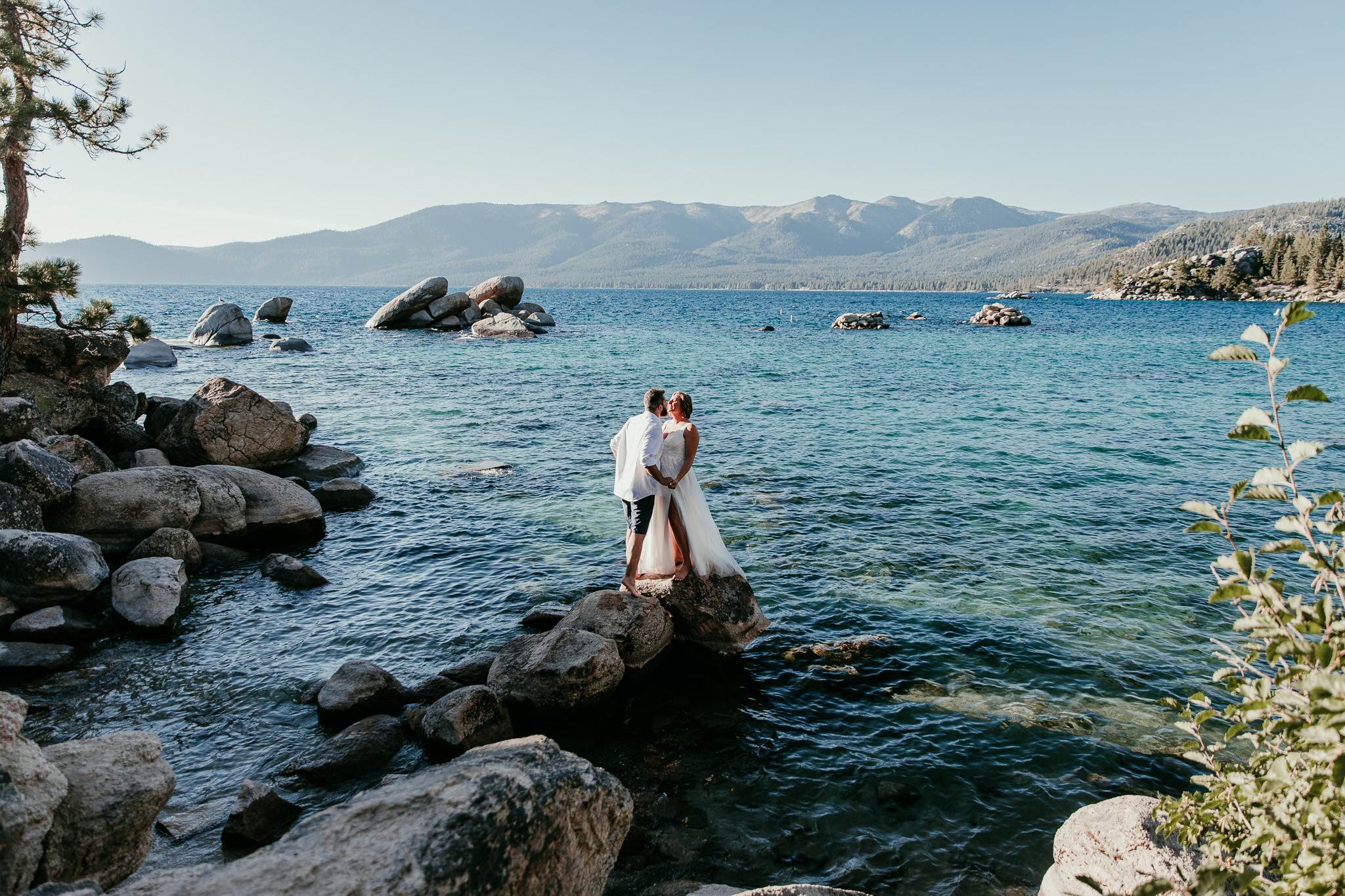 SJ and Dave kissing on a granite rock surrounded by Lake Tahoe’s blue water at Sand Harbor.