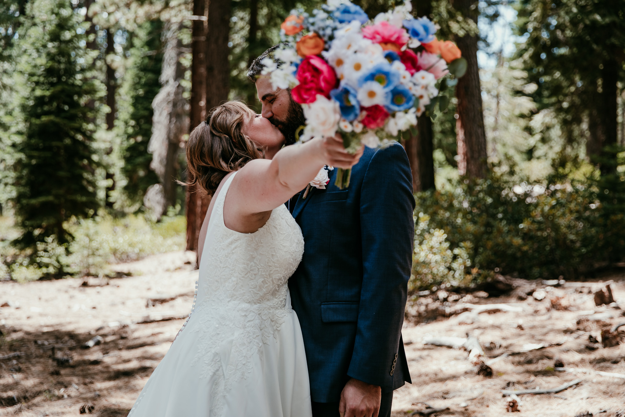 Newlyweds kissing behind a colorful bouquet among the pine trees during their summer Lake Tahoe elopement.