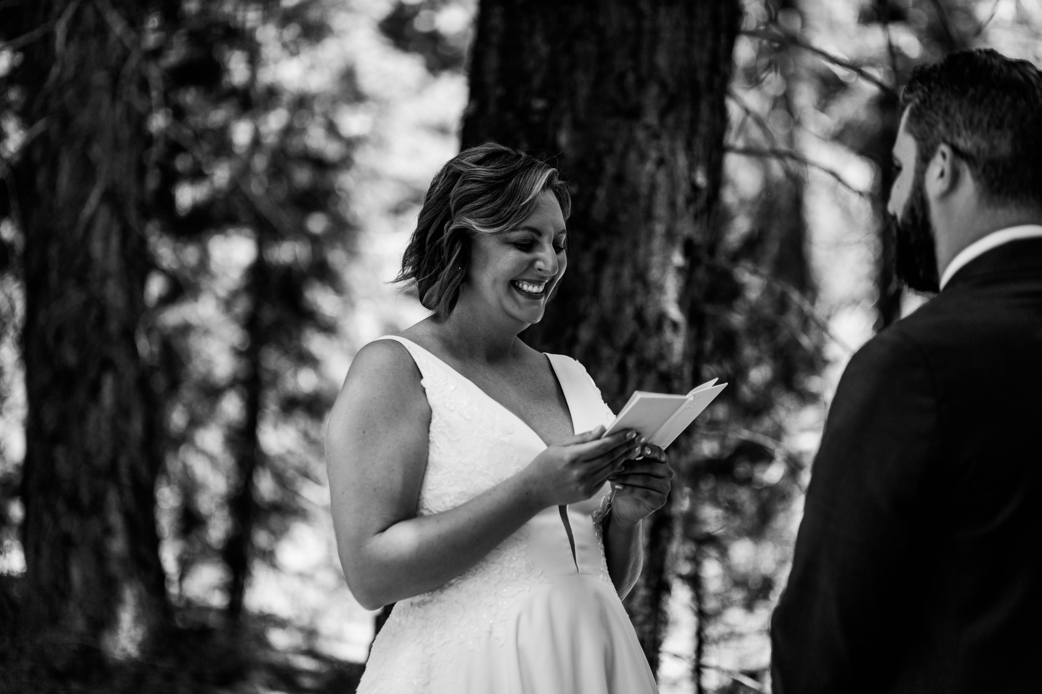 Black-and-white photo of the bride smiling as she reads her vows during their Lake Tahoe forest ceremony.