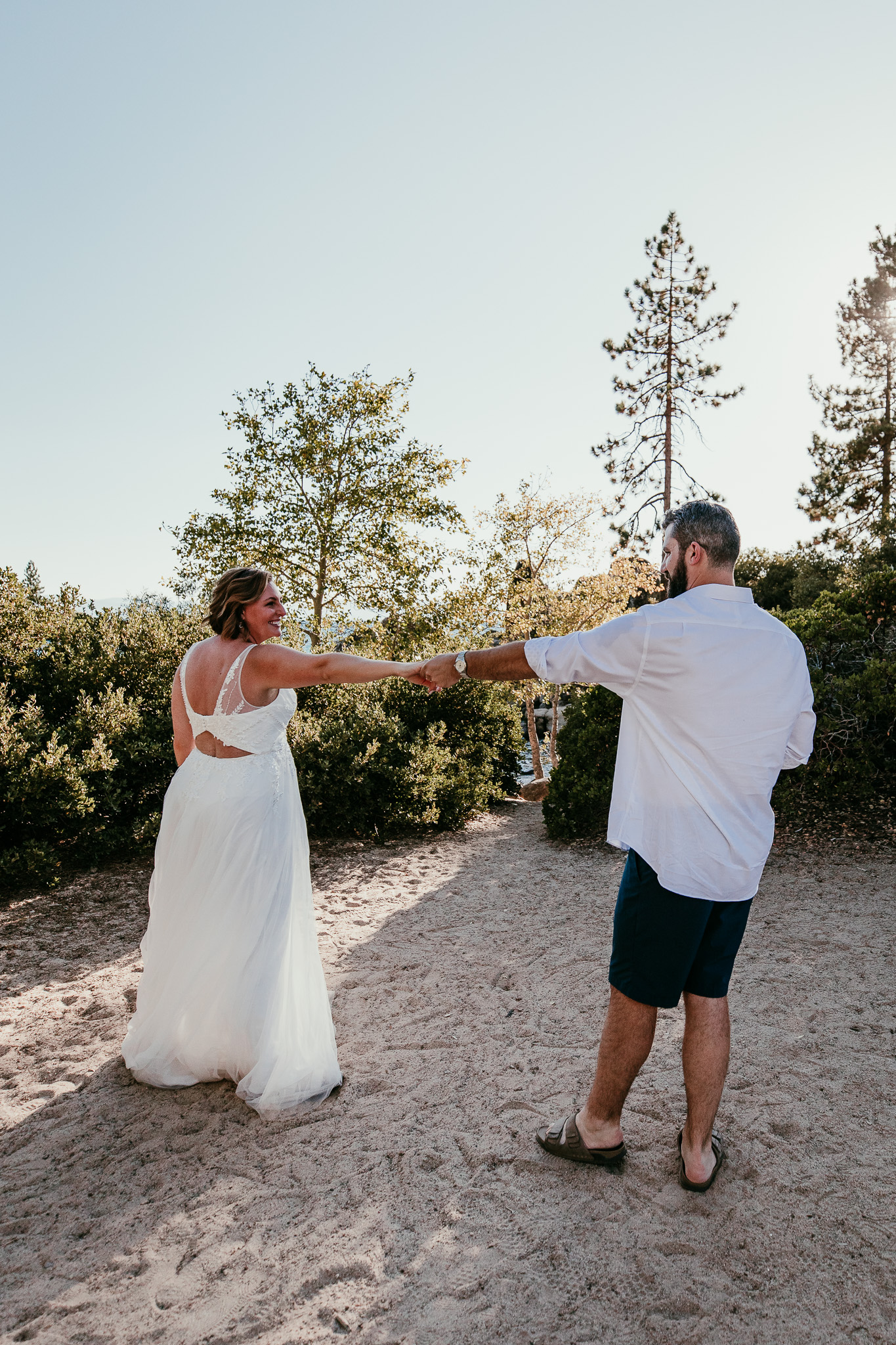 SJ and Dave holding hands with their arms outstretched as they dance barefoot on the sand.