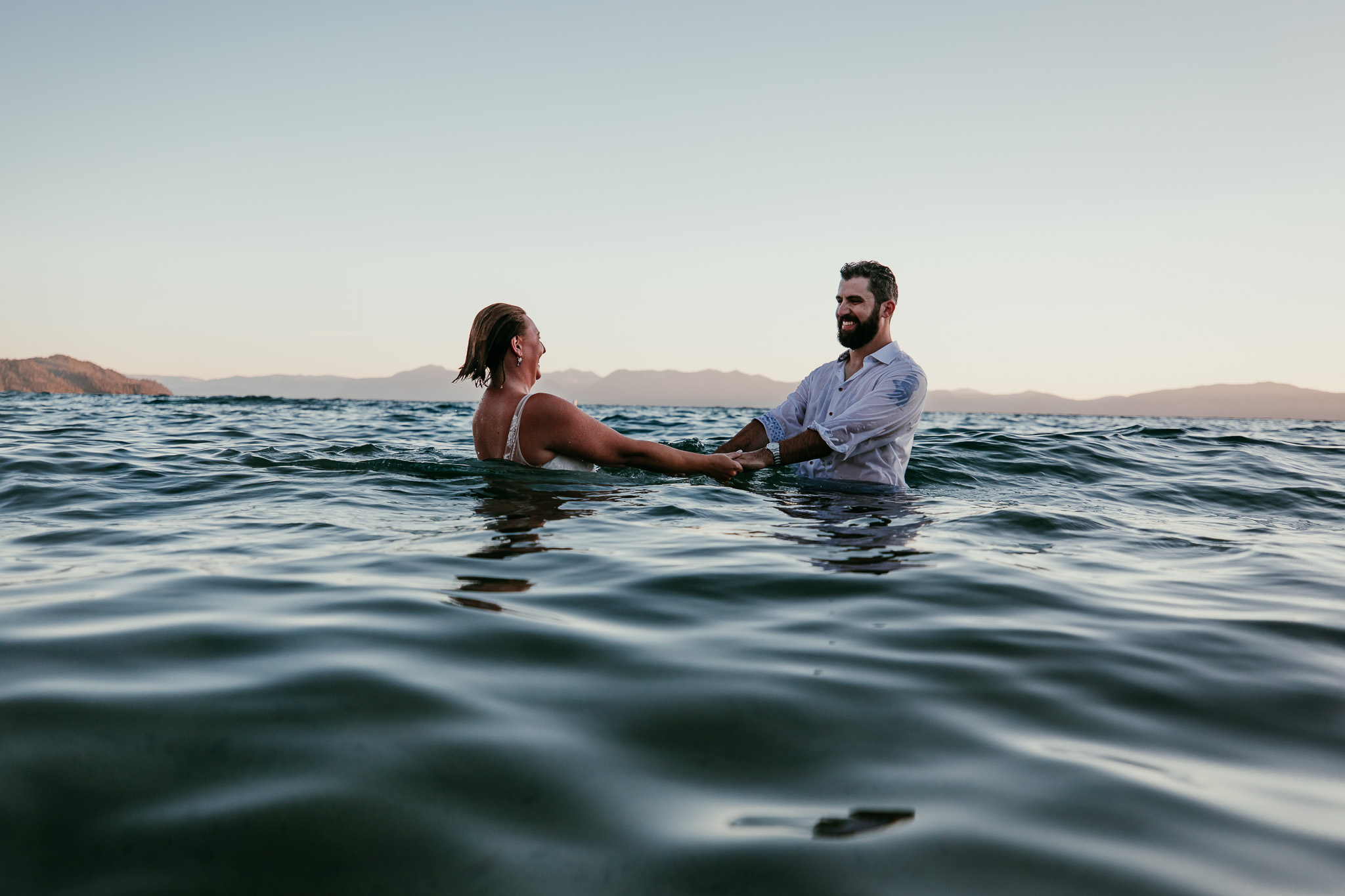SJ and Dave holding hands and smiling while swimming in their wedding clothes.