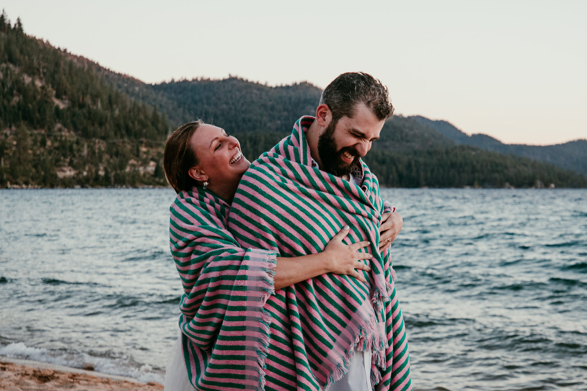 SJ laughing with her head tilted back as she and Dave cuddle under a striped towel.
