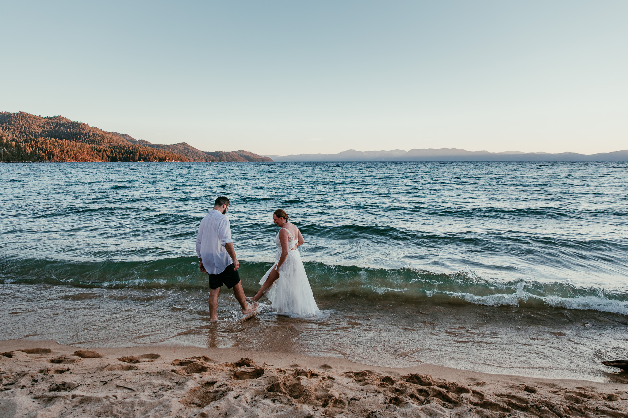 SJ and Dave holding hands in the shallow water as waves splash around their legs.