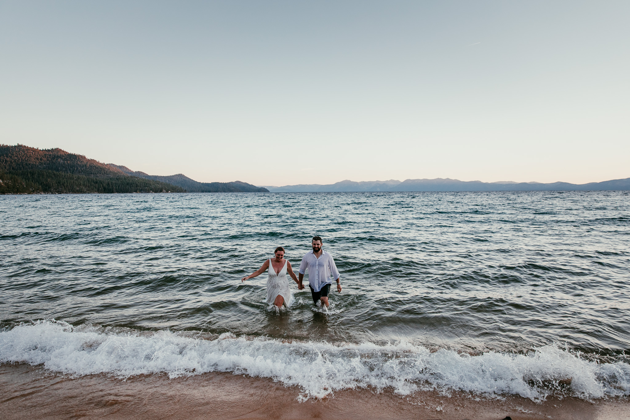 SJ and Dave laughing together in the waves near the beach during their summer elopement.