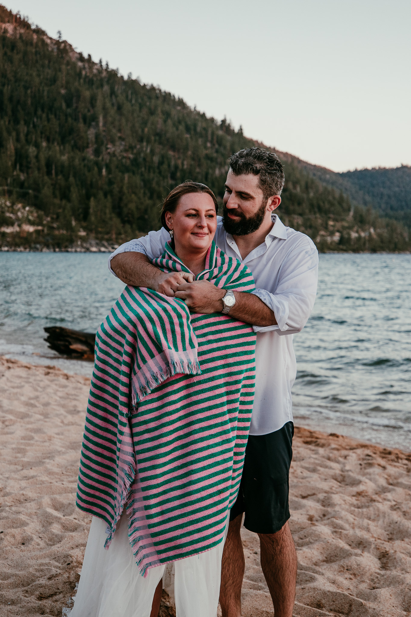 Dave hugging SJ from behind as she wraps herself in a striped towel after their lake swim.