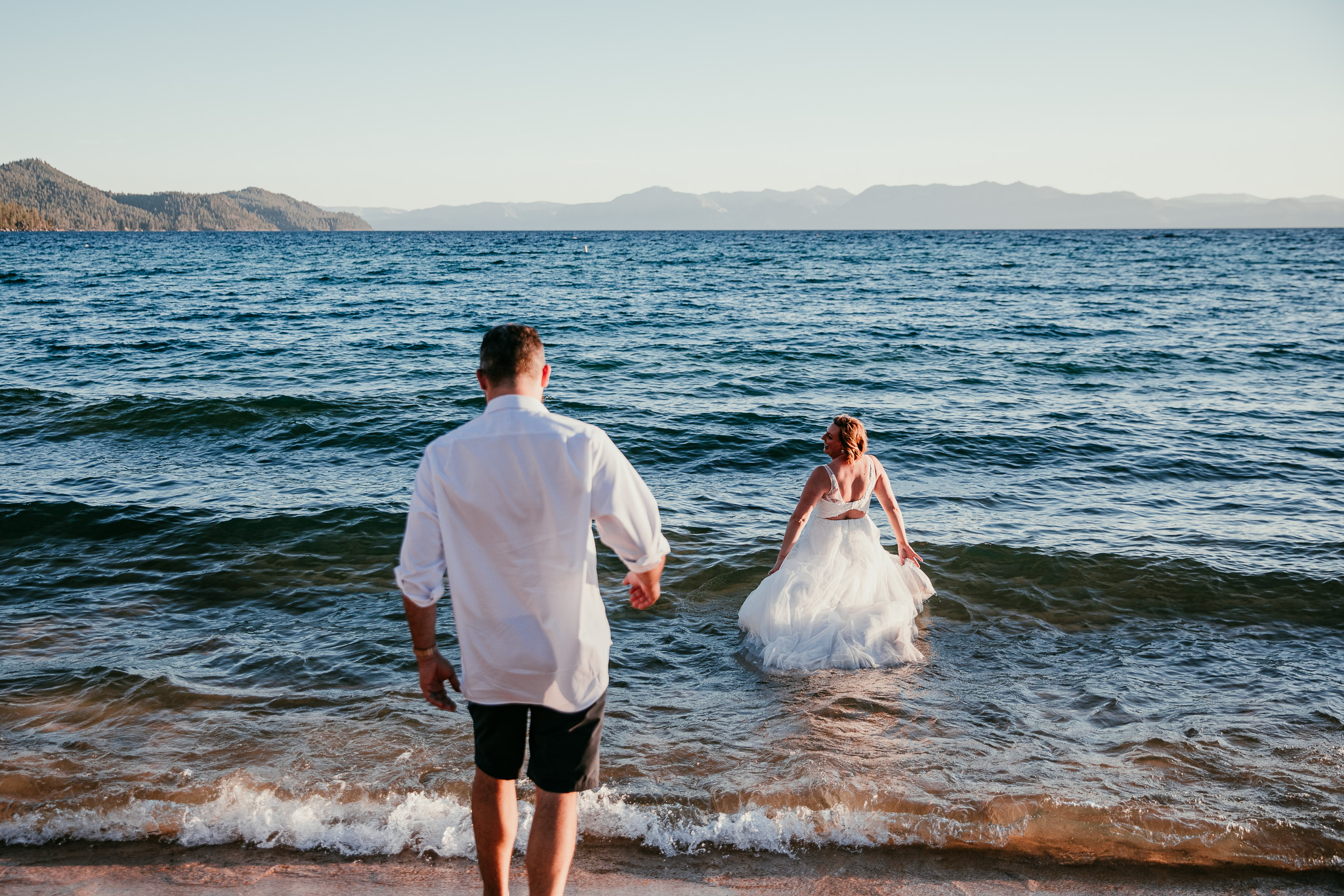 SJ wading into Lake Tahoe in her wedding dress as Dave follows her into the waves.
